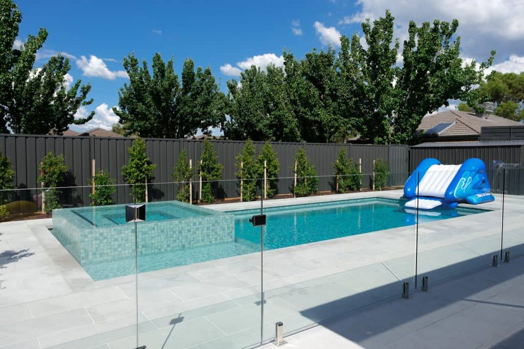 Outdoor swimming pool with safety fencing and water slide in backyard.