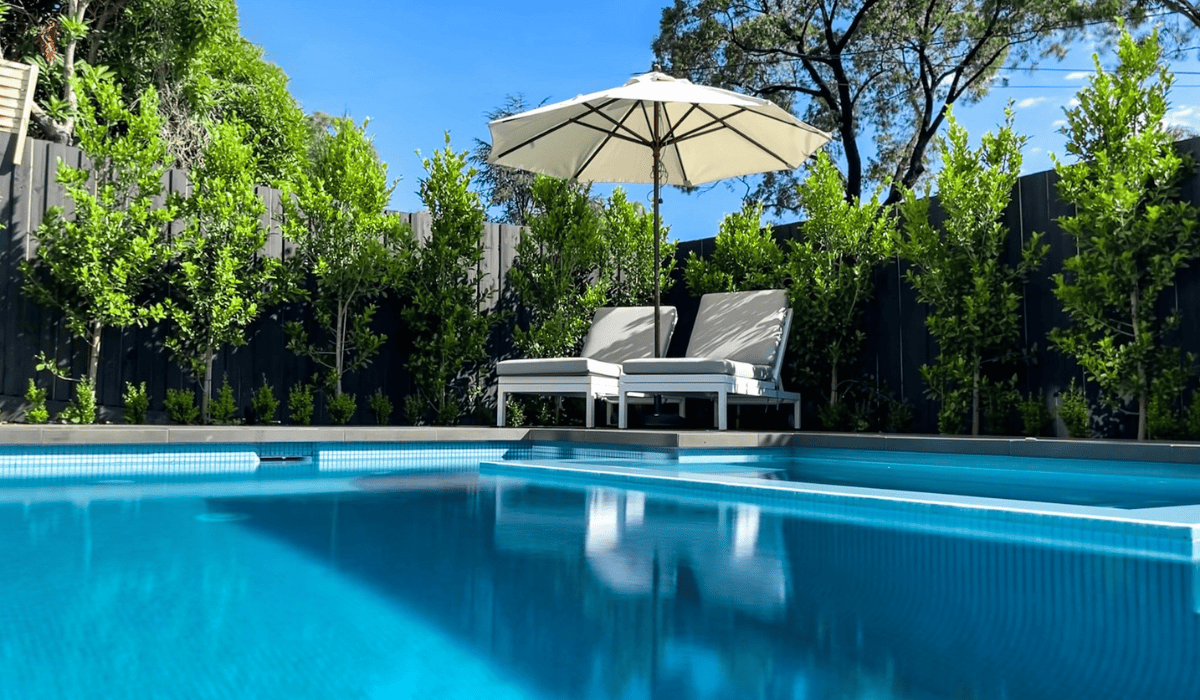 Modern backyard pool with lounge chairs and umbrella under blue sky.