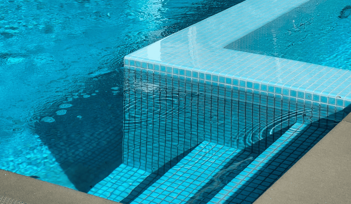 Close-up of a modern tiled swimming pool with steps and clear blue water.