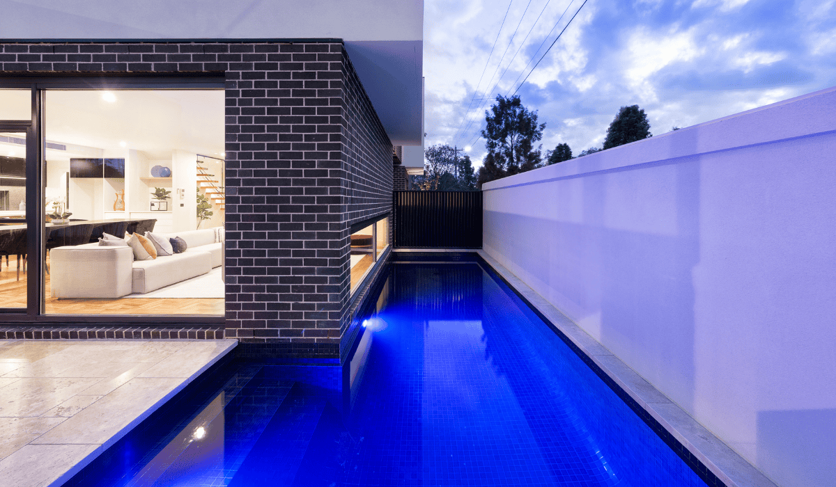 Modern backyard with illuminated swimming pool and sleek white wall.