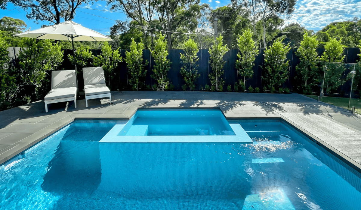 Modern backyard pool with spa and outdoor lounge area in sunny setting.