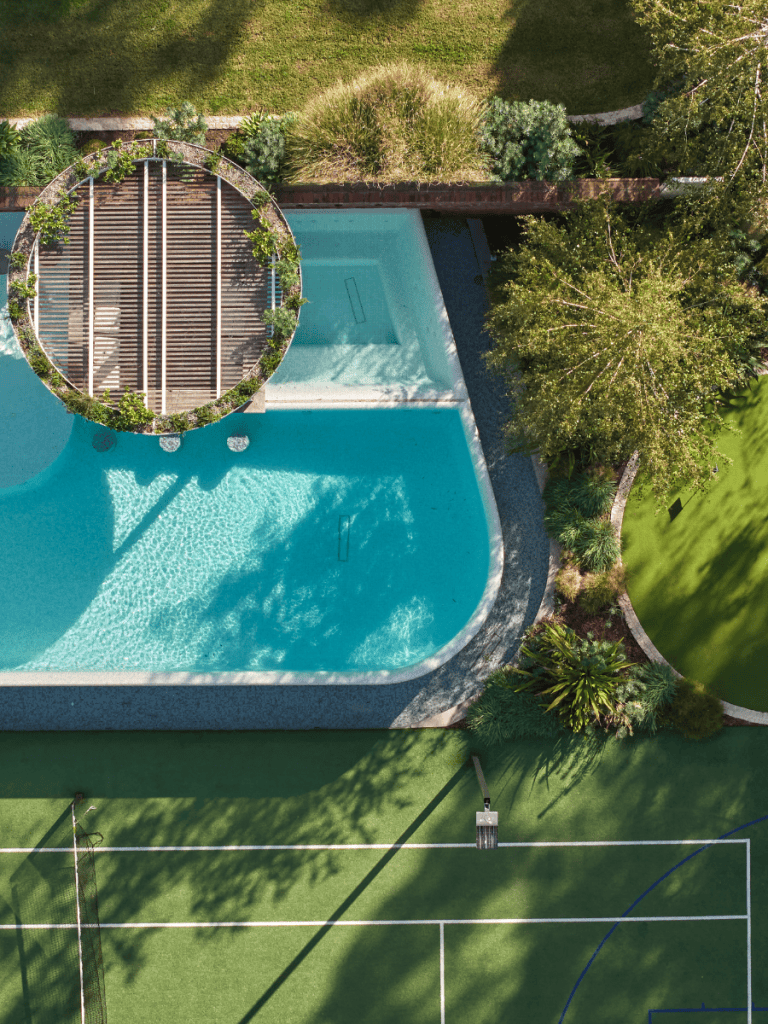 Aerial view of a modern swimming pool with a circular hot tub and surrounding greenery.
