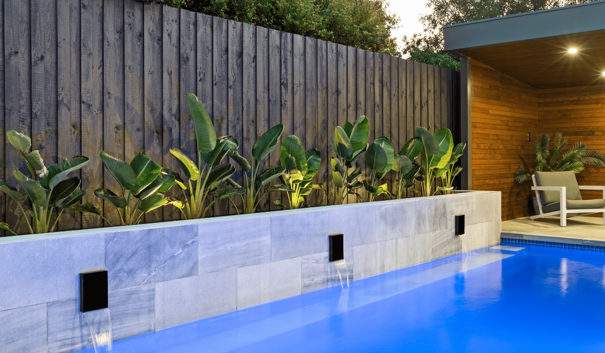 Contemporary backyard pool with water feature and lush garden.