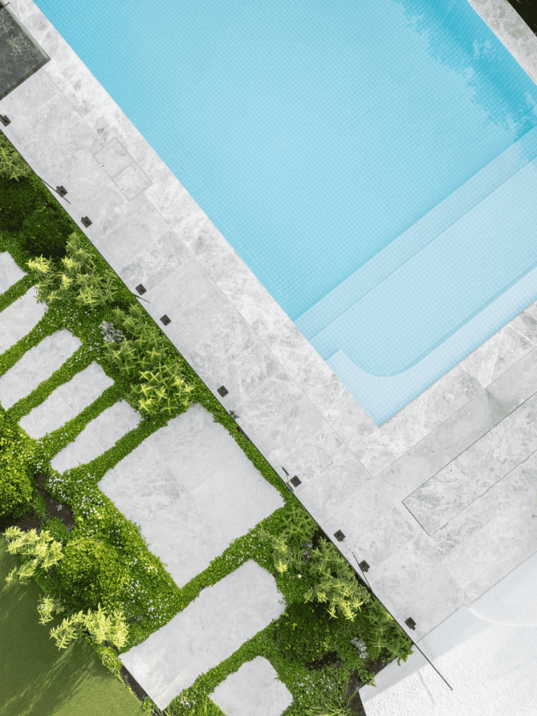 A modern swimming pool with a surrounding stone deck and lush garden landscape.