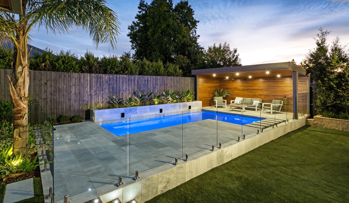 Contemporary backyard pool with glass fencing, outdoor lounge, and garden.