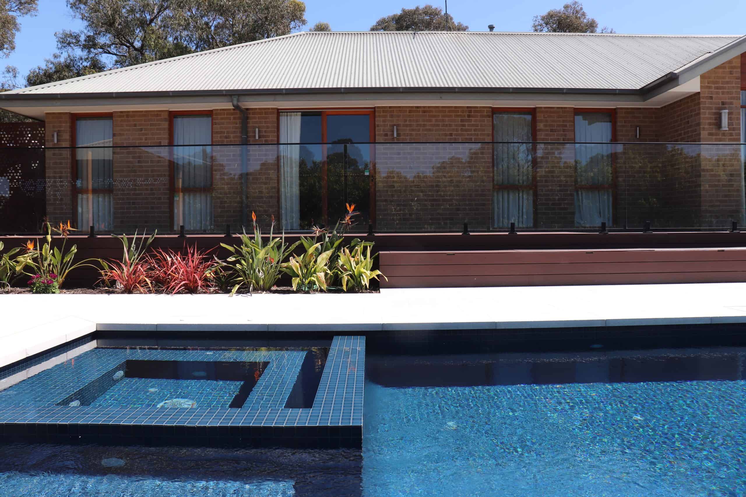 Modern backyard with in-ground swimming pool and spa, surrounded by a house and garden.