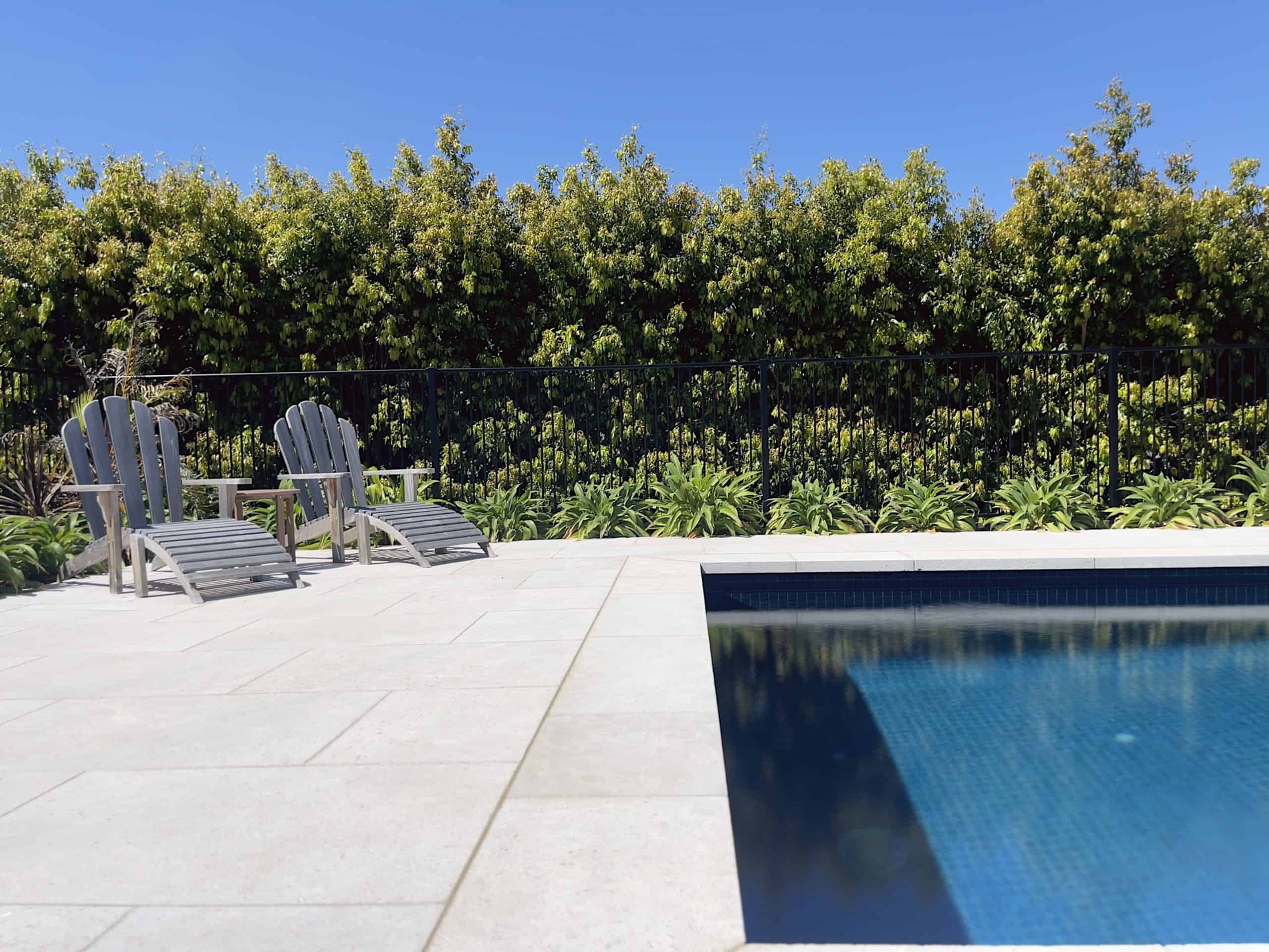 Modern backyard pool with lounge chairs and lush greenery in the background.