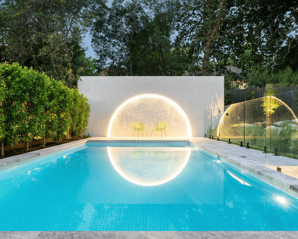 Contemporary backyard pool with LED lighting and glass fencing.