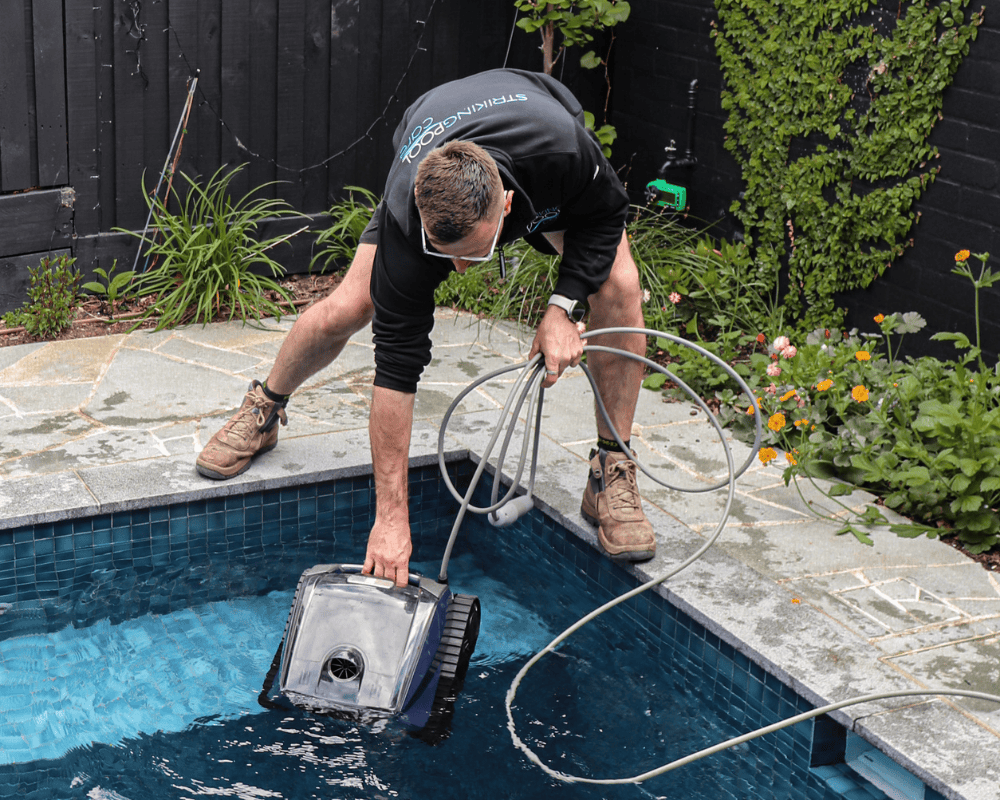 Technician cleaning a backyard swimming pool with a vacuum cleaner.