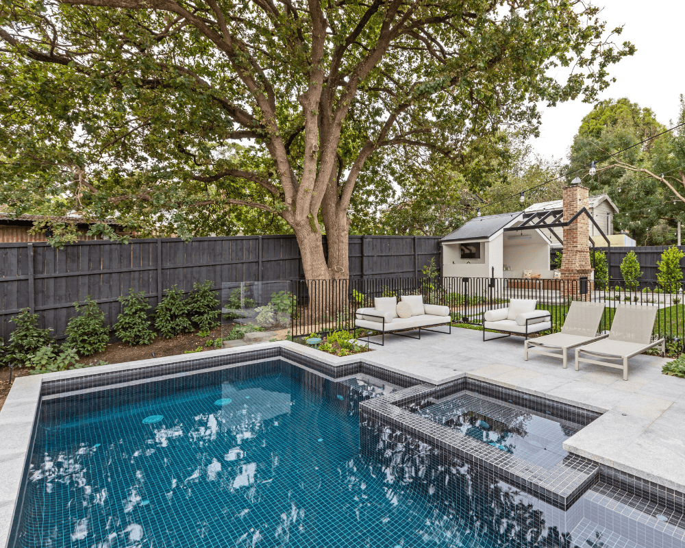 Modern backyard with in-ground pool, hot tub, and outdoor seating area under large tree.