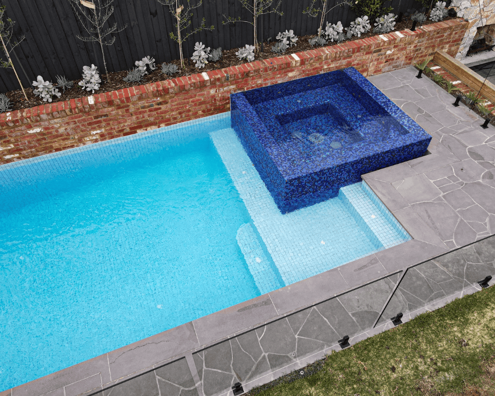 Modern backyard pool with a raised spa and glass fencing in Australia.