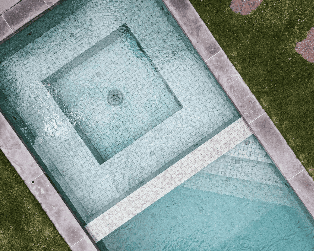 Aerial view of a modern rectangular swimming pool with a built-in spa and surrounding grass.