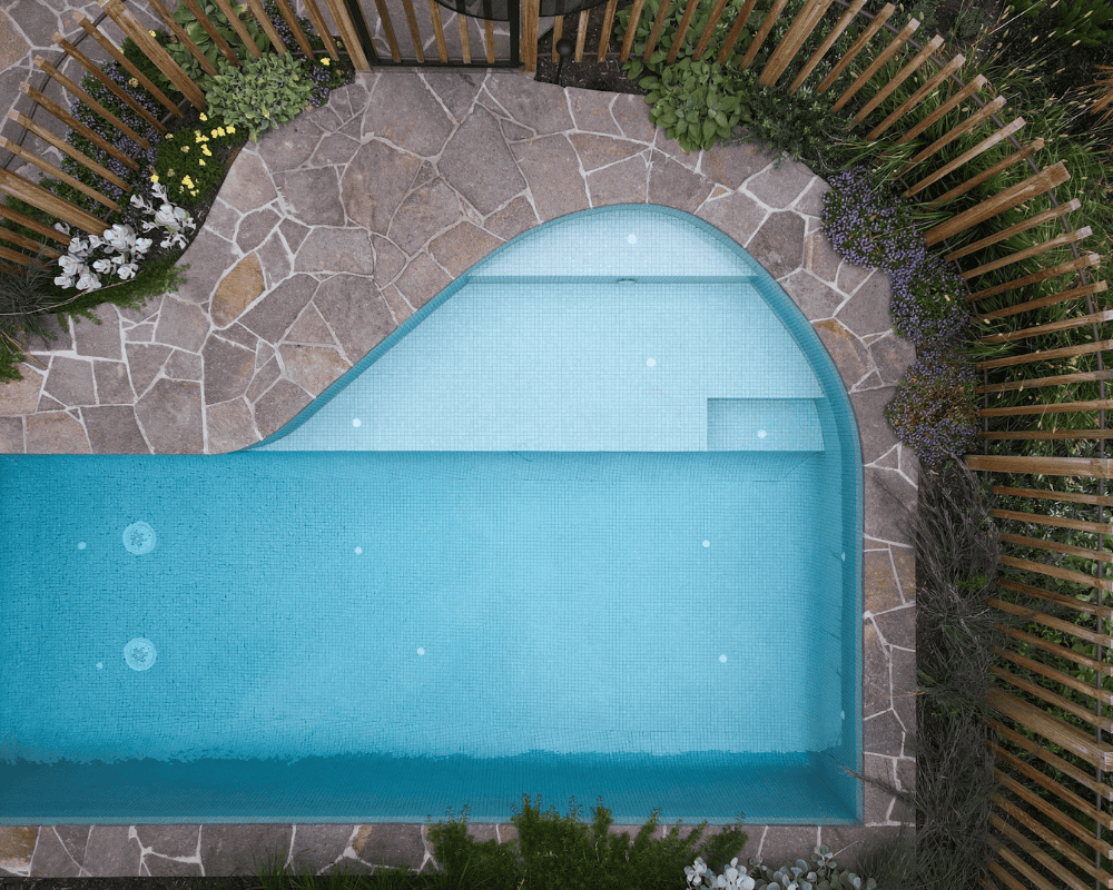 A modern backyard pool with a curved design and stone paving surround.