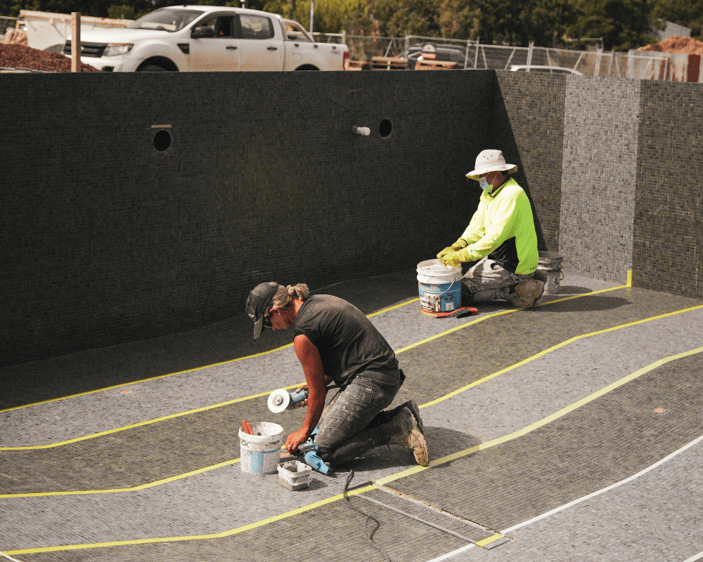 Pool construction workers installing waterproofing membrane at a construction site.