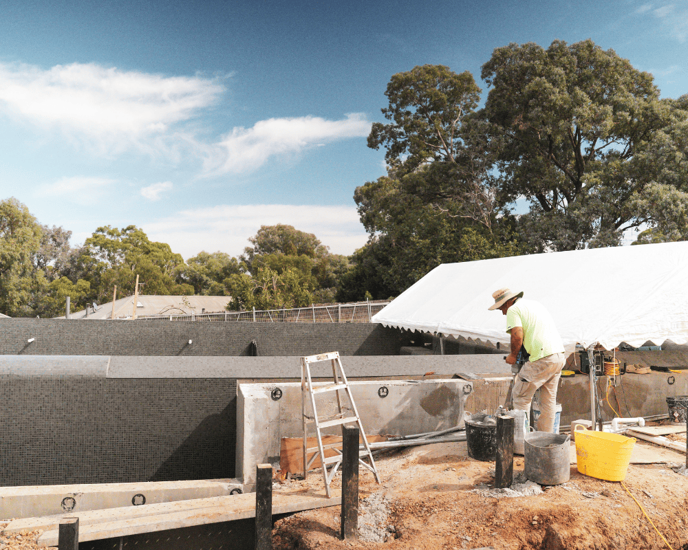 Pool construction site with worker applying waterproofing membrane in Australia.