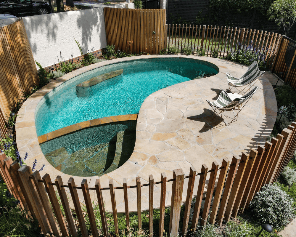 Modern backyard pool with stone deck and wooden fence, perfect for relaxation.